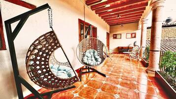 Un patio techado con dos sillas colgantes de mimbre, piso de baldosas y pared de ladrillo.