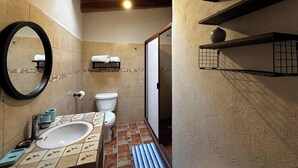 Ein Badezimmer mit einem weißen Waschbecken, einer Toilette, einem Spiegel und Ablagen für Toilettenartikel.
