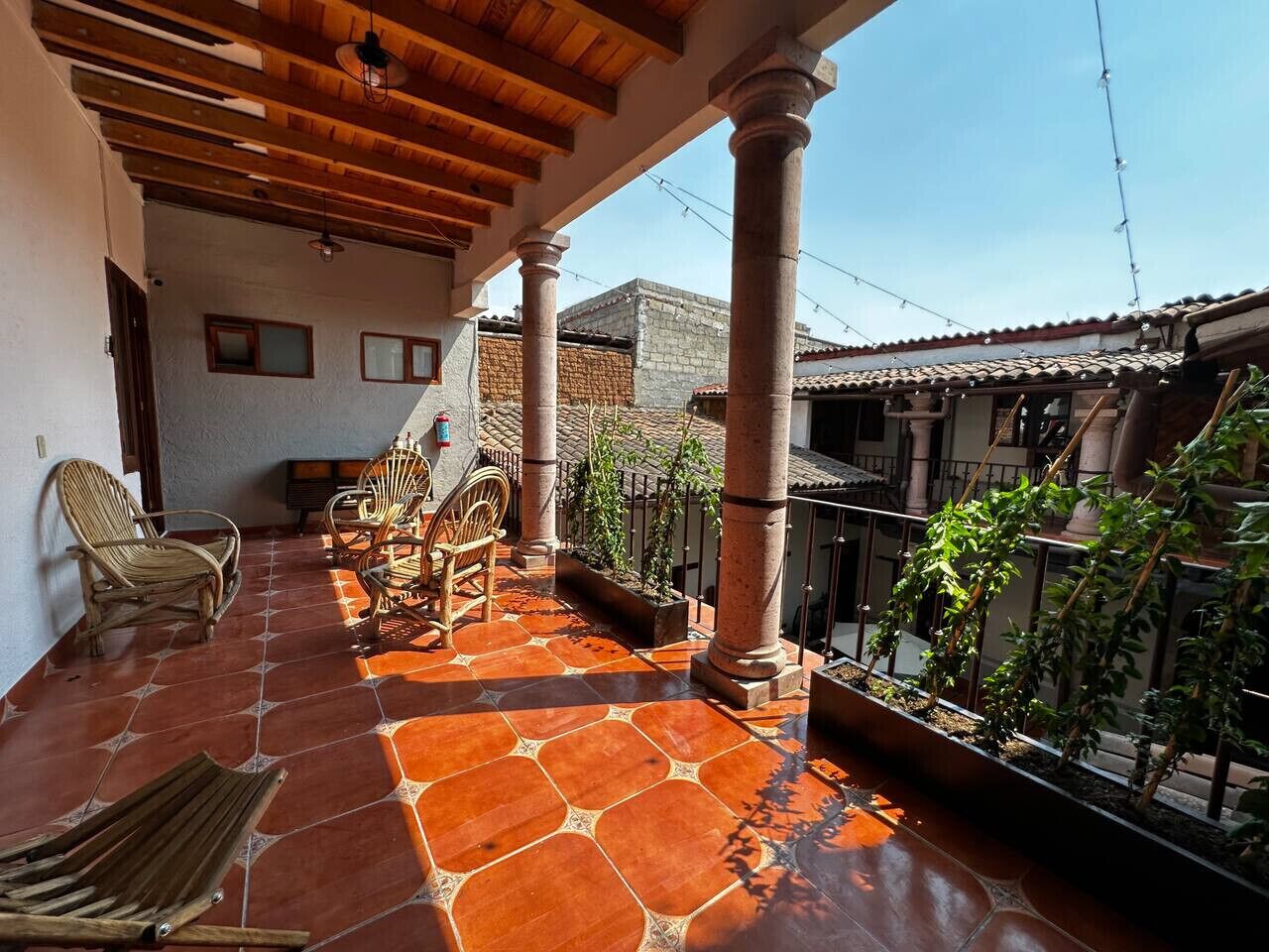 A covered patio with terracotta tiles, wooden furniture, and a view of neighboring buildings.
