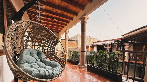 A hanging chair with a cushioned seat and backrest, a tiled floor, and a railing with potted plants. - Hotel Room, one block from the Lake centr 3 (Valle de Bravo)