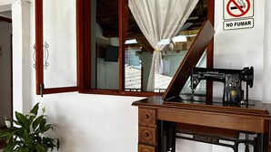 Un bureau en bois, une machine à coudre Singer, une plante en pot et une fenêtre avec un rideau.