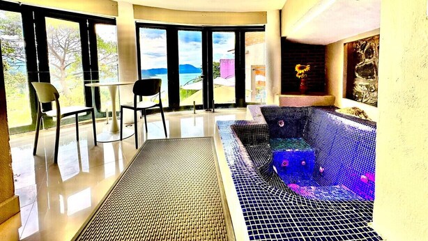 Een moderne kamer met een glazen wand, een zithoek met een blauw mozaïekbad en uitzicht op zee.
