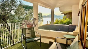 Un balcón con vistas a un lago y montañas, una piscina pequeña y mobiliario exterior.