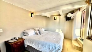 Un dormitorio con una cama grande, una mesita de noche, una lámpara y una ventana.
