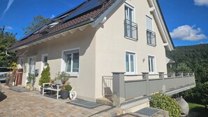 A two-story house with a sloped roof, solar panels, and a balcony. - Modern vacation apartment in a very beautiful location, surrounded by forests and hiking trails! (Heimbuchenthal)