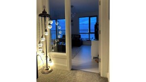 A hallway with a tall, ornate floor lamp and a view of a living area through a glass door. - Atlantic Views & Irish Charm (Ballycotton)