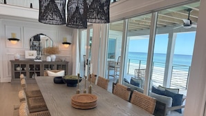 A dining area with a long wooden table, wicker chairs, and a view of the ocean.