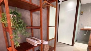 A wooden shelf unit with towels and a plant, a bathroom with a sink and mirror, and a door leading to another room.