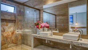 Un baño moderno con cabina de ducha de vidrio, encimera de mármol y un espejo grande.
