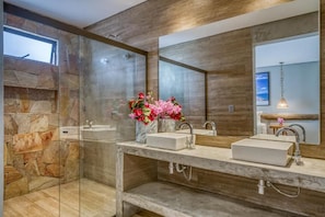 A modern bathroom with a glass shower enclosure, a marble countertop, and a large mirror. - Villa Italiana (São Miguel dos Milagres)