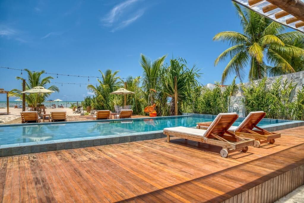 A poolside area with lounge chairs, umbrellas, and palm trees.