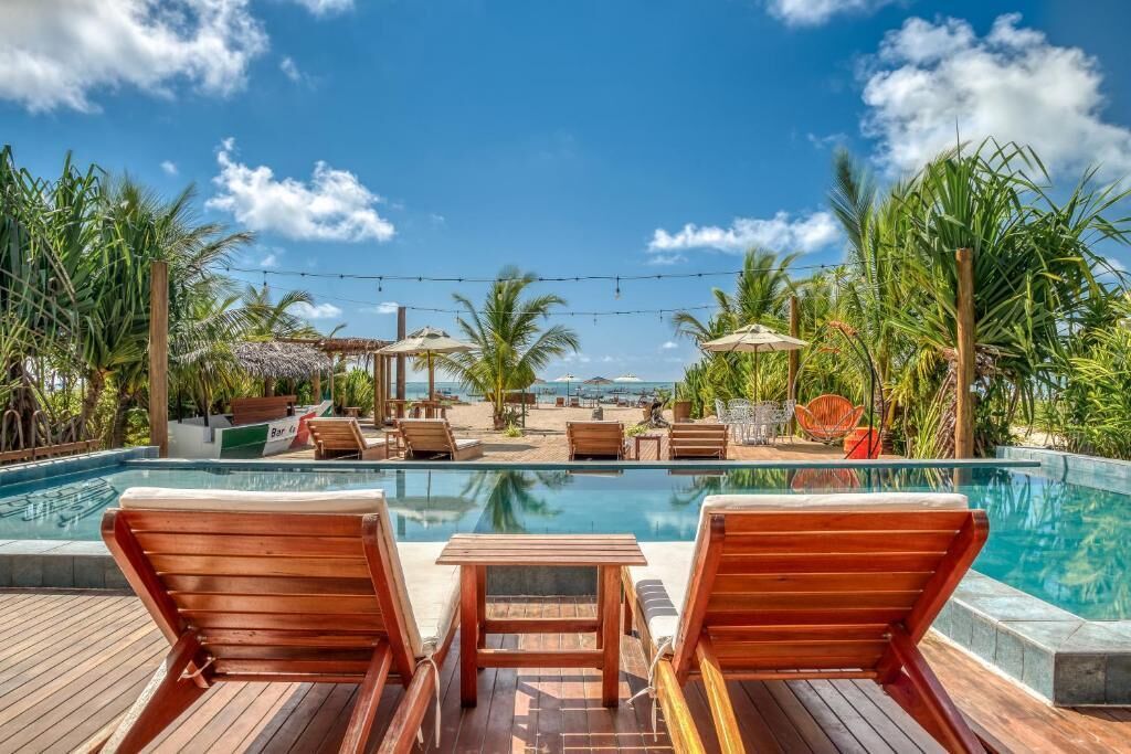 Ein Poolbereich mit Holzliegen, einem kleinen Tisch und Sonnenschirmen.