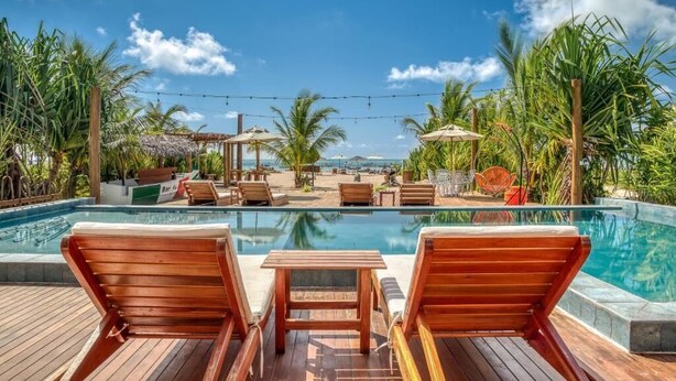 Un área de piscina con sillones de madera, una pequeña mesa y sombrillas.
