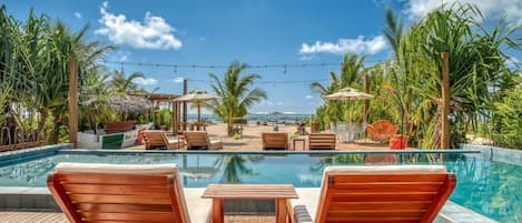 Un área de piscina con sillones de madera, una pequeña mesa y sombrillas.