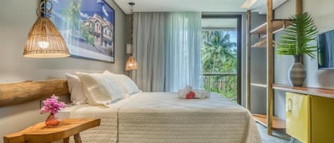 A hotel room with a large bed, a wooden headboard, a small table with a vase, a television, and a balcony with a view of palm trees.
