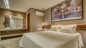 Habitación de hotel con una cama grande, cabecera de madera, un espejo amplio, aire acondicionado instalado en la pared y un cuadro sobre la cama.