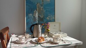 A dining table with a floral tablecloth, a teapot, cups, saucers, and a plate with a slice of cake. - Cristina's House (Martellago)