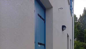 A blue door with a metal latch, a white wall, and a small window with a light fixture. - Cristina's House (Martellago)