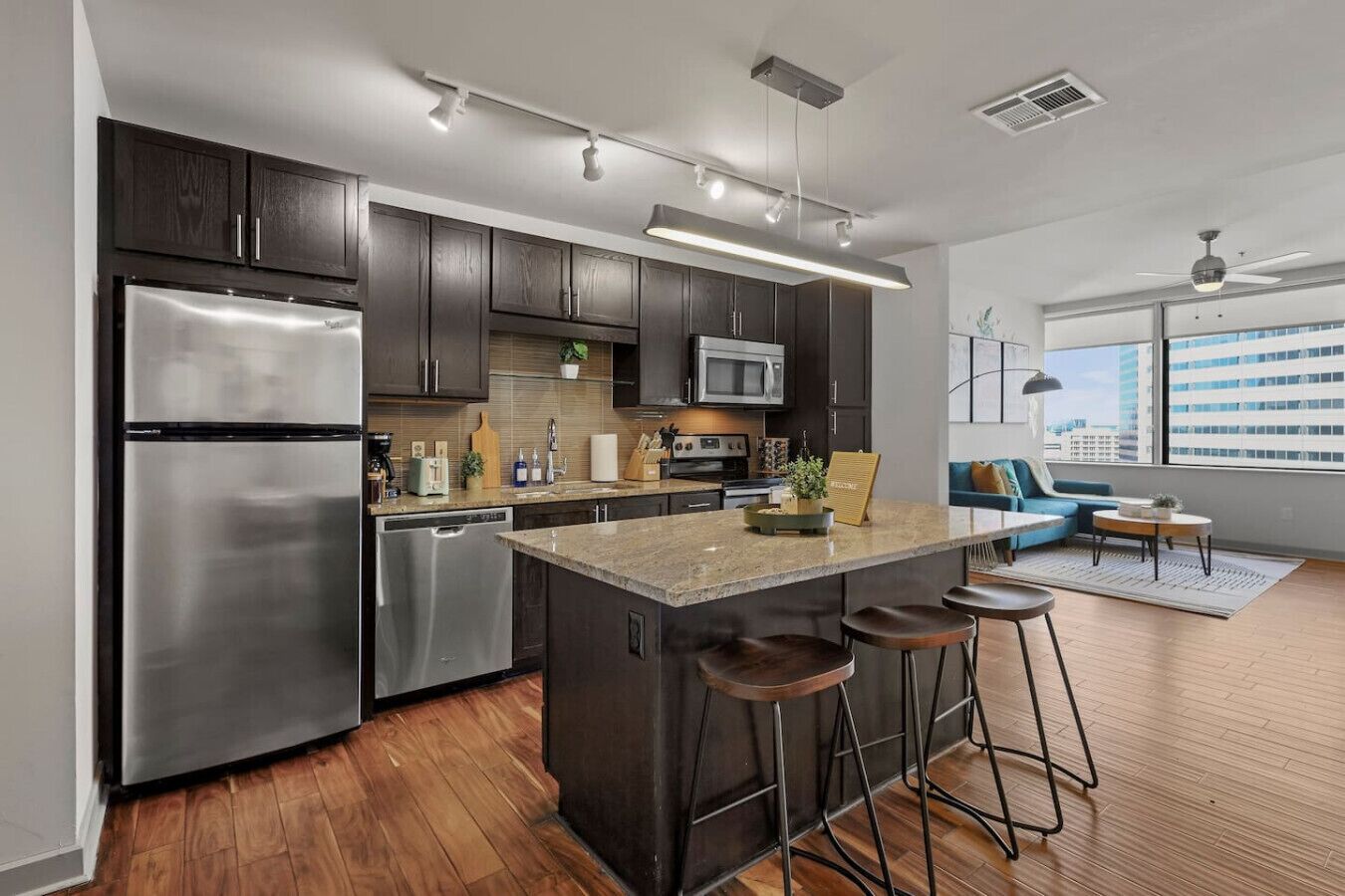 A modern kitchen with dark cabinets, stainless appliances, and a central island with stools.