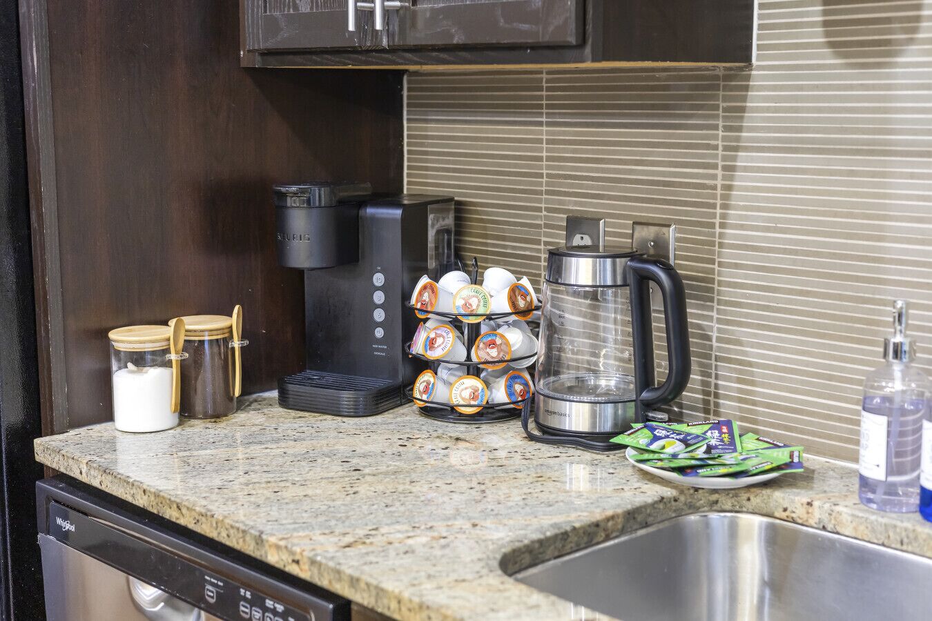 A kitchen with a coffee maker, a coffee pot, a dish rack with cups, and a dish soap bottle.