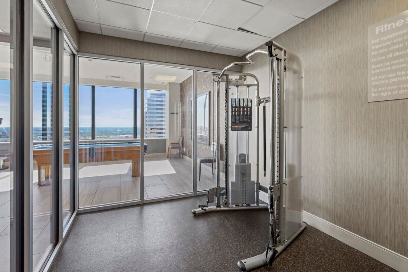 A fitness area with a weight machine, large windows, and a view of the city.