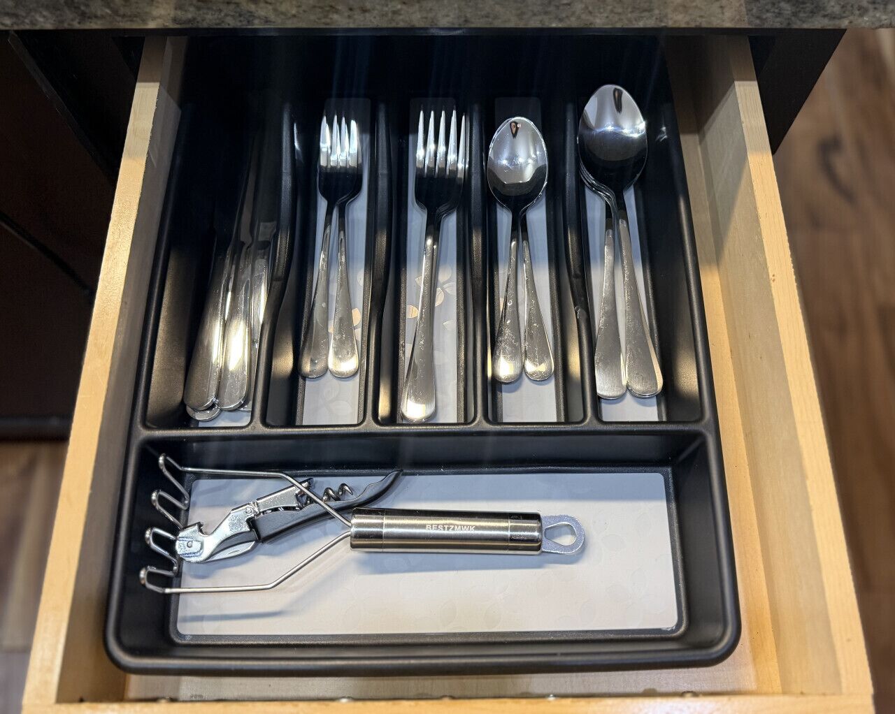 Een lade met een serviesbestek, inclusief vorken, messen en lepels, evenals een blikopener en een flesopener.