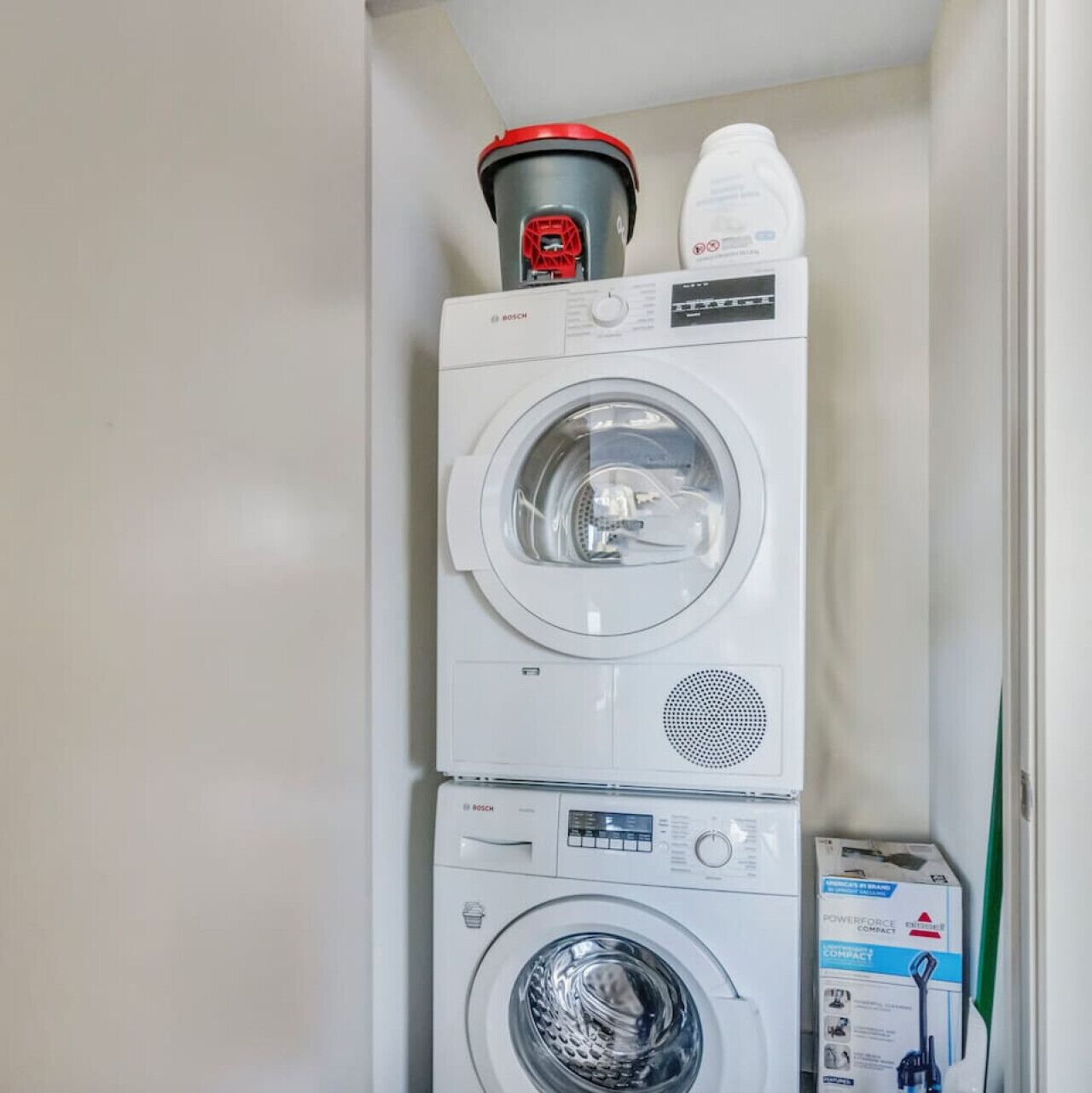 Un appareil combiné lave-linge et sèche-linge de la marque Bosch, avec un dessus rouge et un modèle de sèche-linge compact Powerforce.