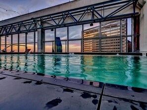 A swimming pool with a view of a modern building with large windows and a metal structure overhead.