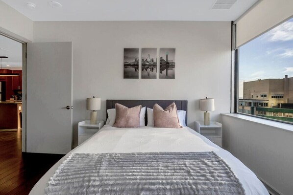 A modern hotel room with a large bed, two bedside tables, and a cityscape view through the window.