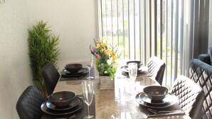A dining table set with black plates, bowls, and glasses, surrounded by black cushioned chairs. A wooden side table holds a vase with flowers. - Luxury 3 bedroom house in Harlow, Essex (Harlow)
