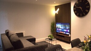 A modern living room with a large wall clock, a flat-screen TV, and a sofa. - Luxury 3 bedroom house in Harlow, Essex (Harlow)