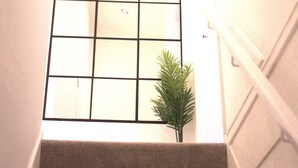 A staircase with carpeted steps leading to a landing with a grid-patterned window. - Luxury 3 bedroom house in Harlow, Essex (Harlow)