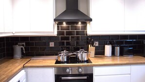 A kitchen with white cabinets, a black tiled backsplash, a stainless steel range hood, and a wooden countertop. - Luxury 3 bedroom house in Harlow, Essex (Harlow)