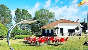 A grassy outdoor area with a white building, red chairs, and a large umbrella structure.