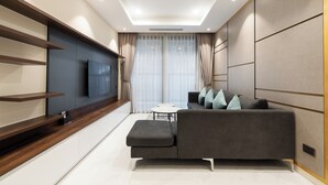 A modern living room with a grey sofa, a flat-screen TV, and a wooden shelf.