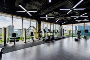 Uma academia moderna com diversos equipamentos de exercício, amplas janelas que oferecem vista da cidade e um layout espaçoso.