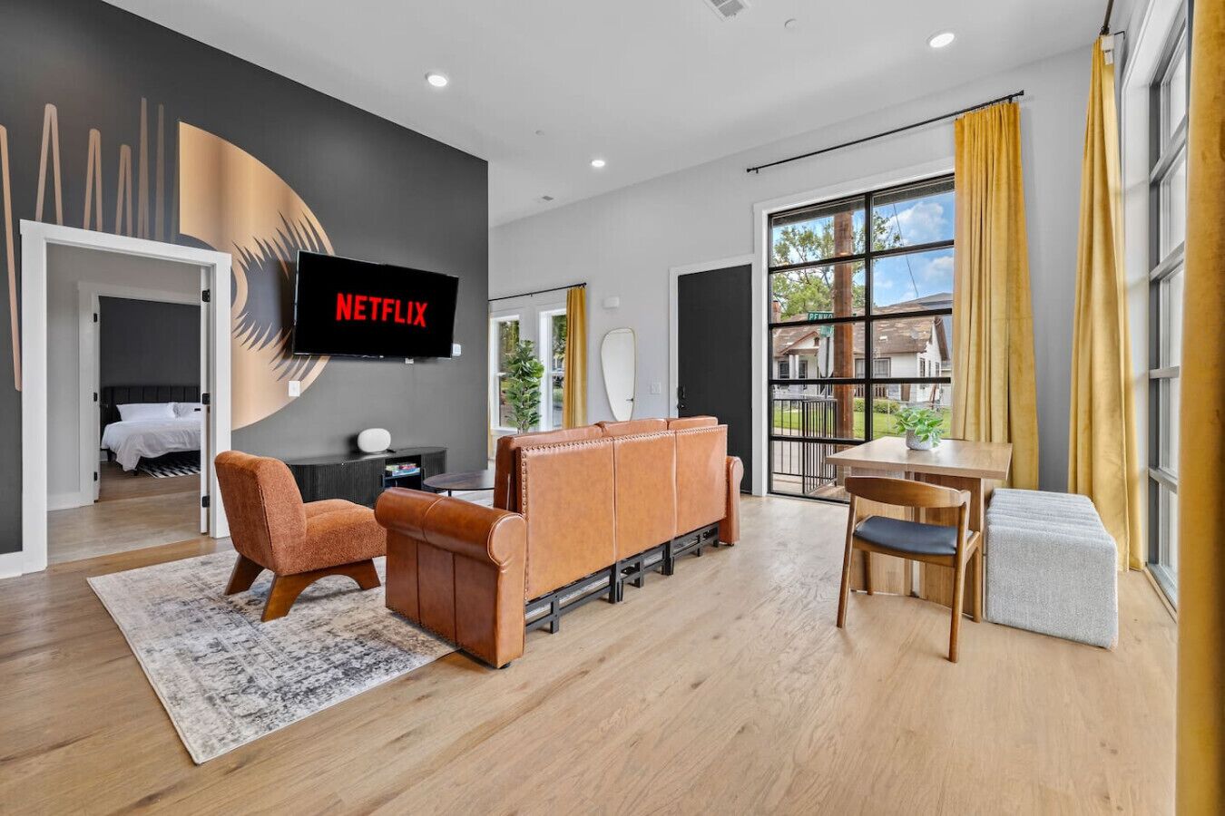 Un salon moderne avec un canapé, un fauteuil et un coin repas comprenant une table et des chaises. Un téléviseur est fixé au mur et affiche le logo de Netflix.