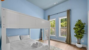Una cama litera en una habitación con paredes azules, un ventanal grande y una planta en maceta.