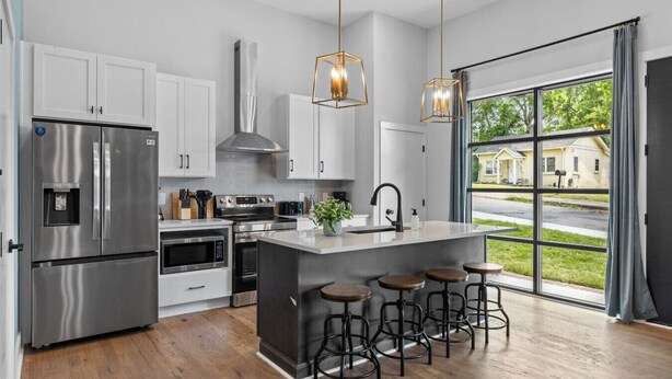 Una cocina moderna con electrodomésticos de acero inoxidable, una isla central con taburetes y ventanas amplias que ofrecen vistas del vecindario.