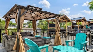 A covered outdoor deck with wicker furniture and turquoise chairs, featuring a pergola with curtains.