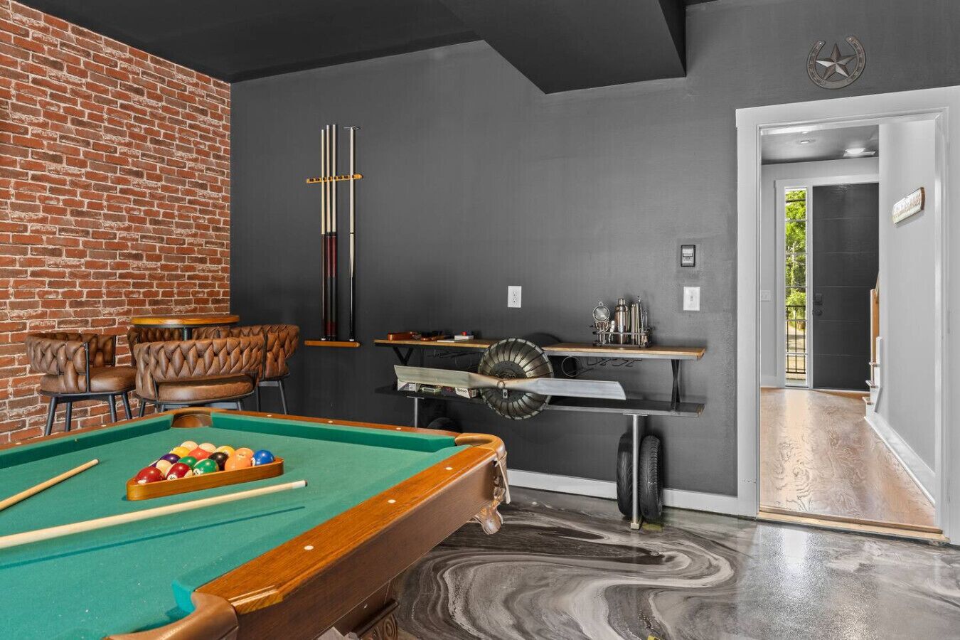 A billiards room with a pool table, leather chairs, and a brick wall.