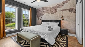 Een slaapkamer met een groot bed, een bankje, een plafondventilator en een bakstenen muur.