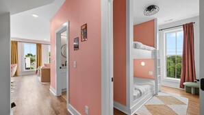 Une chambre d’hôtel moderne avec un lit superposé, une grande fenêtre avec des rideaux, un plancher en bois et un couloir menant à une salle de bain.