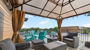Un espace extérieur aménagé avec une terrasse couverte, du mobilier en osier, une vue sur la ville et une plateforme en bois.