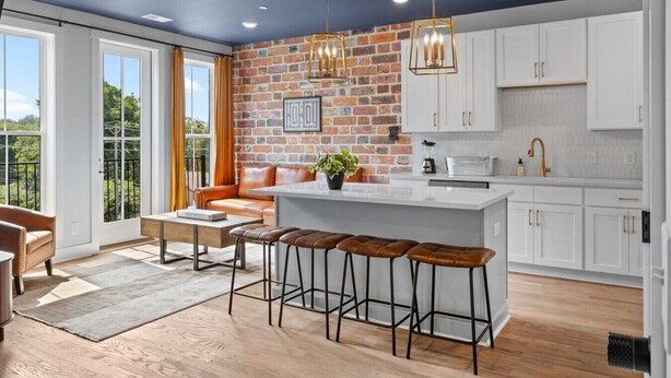 A modern kitchen with a brick accent wall, white cabinets, and a central island with stools. - NASH Bach Pad 3-Bedroom Penthouse near Downtown Nashville (Sleeps 12) (Nashville)