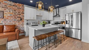 A modern kitchen with a central island, stainless steel appliances, and a brick accent wall. - NASH Bach Pad 3-Bedroom Penthouse near Downtown Nashville (Sleeps 12) (Nashville)