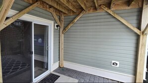 Eine überdachte Veranda mit einer Schiebeglastür, Holzbalken und einem Metalldach.