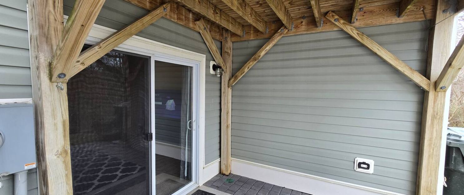 Une véranda couverte avec une porte-fenêtre coulissante, des poutres en bois et un toit en métal.