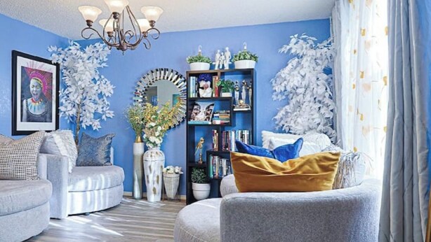 Un soggiorno con una parete blu, un lampadario, una libreria e due alberi artificiali bianchi.