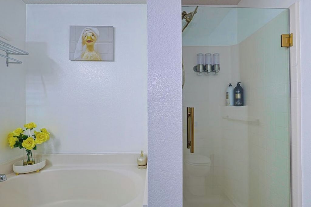 A bathroom with a bathtub, a shower, and a toilet. There is a framed picture on the wall and a vase with yellow flowers on the floor.